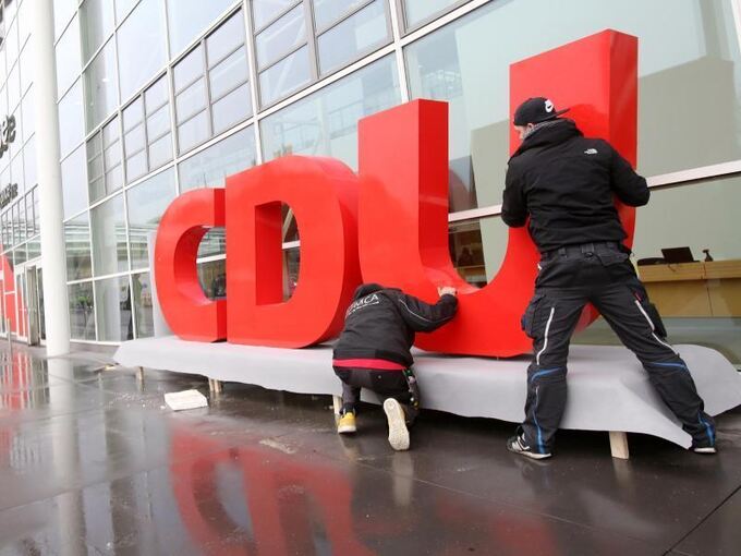 Arbeiter montieren ein CDU-Logo vor einer Messehalle