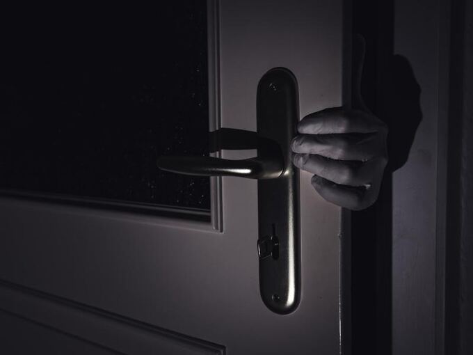 Eine Hand greift im Dunkeln durch eine leicht geöffnete Tür