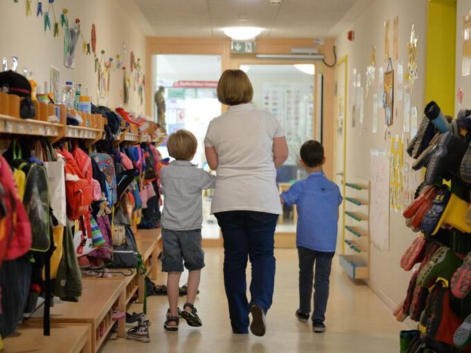 Frau geht mit zwei Kindern über den Flur eines Kindergartens