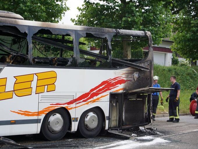 Feuerwehrmänner stehen an einem ausgebrannten Reisebus