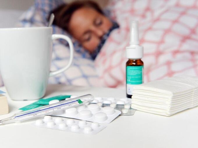 Medikamente und ein Fieberthermometer liegen auf einem Nachttisch