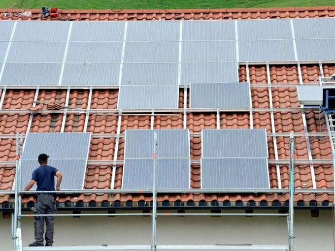 Ein Arbeiter installiert auf einem Dach eine Solaranlage