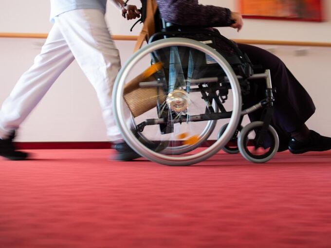 Ein Pfleger schiebt eine Bewohnerin mit einem Rollstuhl