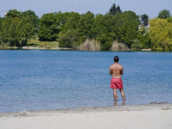 Ein Mann steht am Ufer eines Badesees mit den Füßen im Wasser