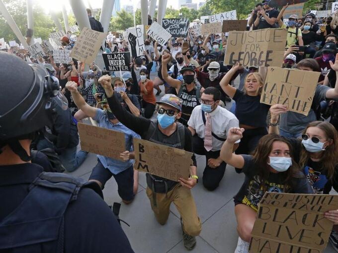 Demonstranten knien bei einem Protest vor einem Polizisten