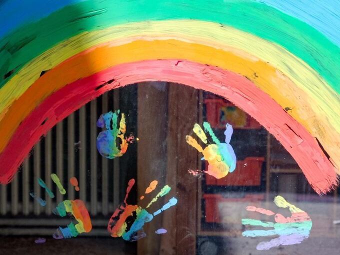 Kinderhände und ein Regenbogen sind durch eine Scheibe zu sehen