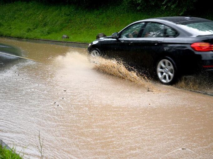 Nach einem Gewitterregen fährt ein Auto durch eine große Pfütze