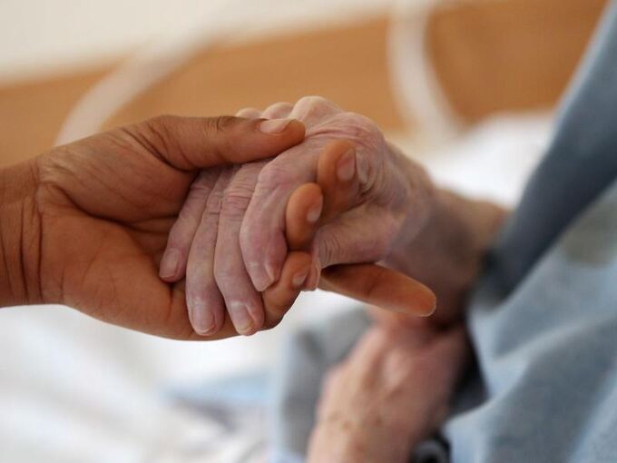 Eine Pflegerin hält in einem Altenheim die Hand einer Bewohnerin