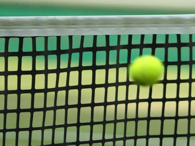 Ein Tennisball fliegt vor das Netz