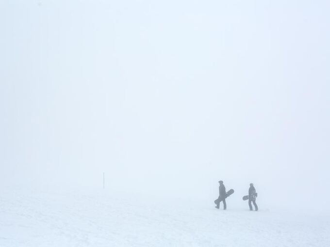 Zwei Snowboarder gehen im dichten Nebel durch den Schnee