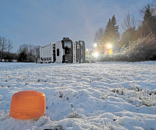Ein Mülllaster liegt umgekippt auf einem verschneiten Stück neben einer Straße bei Bretzfeld. Auf eisglatter Fahrbahn war der Lastwagen von der Straße gerutscht. Foto: Julian Buchner/dpa