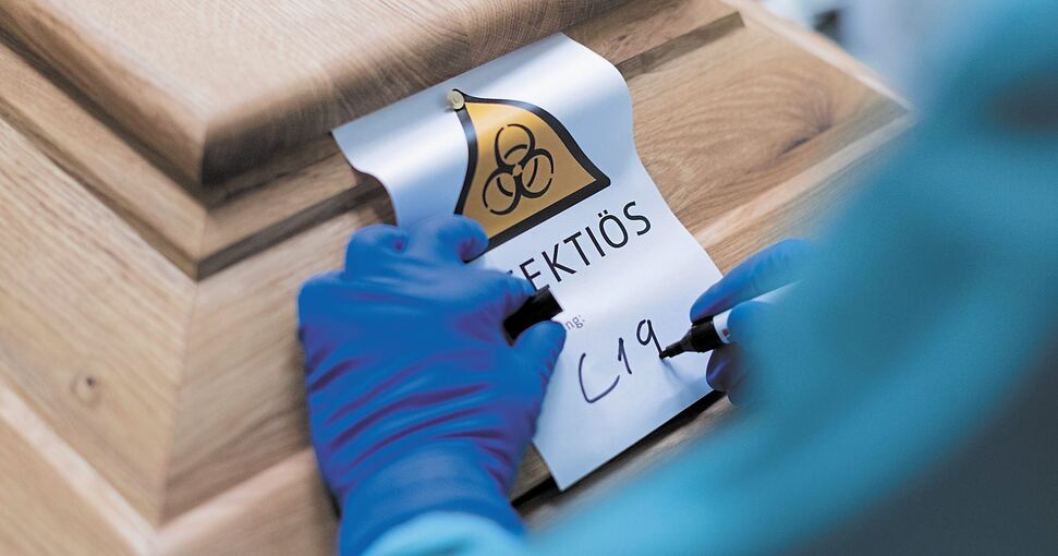 Ein Bestattungsunternehmer schreibt „C19“ auf ein Schild mit dem Hinweis „Infektiös“ auf einen Sarg mit einem Corona-Toten. Foto: Rolf Vennenbernd/dpa