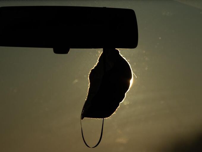 Eine FFP2-Maske hängt vor der aufgehenden Sonne in einem Auto