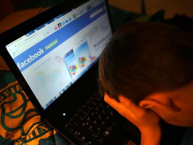 Ein Junge vergräbt vor seinem Laptop sein Gesicht in den Händen
