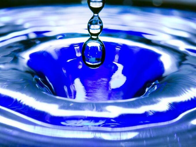Ein Wassertropfen fällt in eine blaue Wasserschüssel