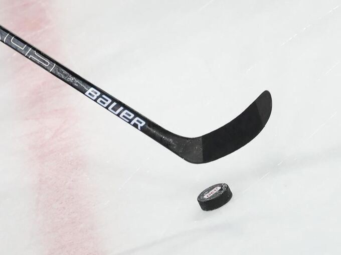 Ein Puck liegt vor einem Eishockey-Schläger auf dem Eis