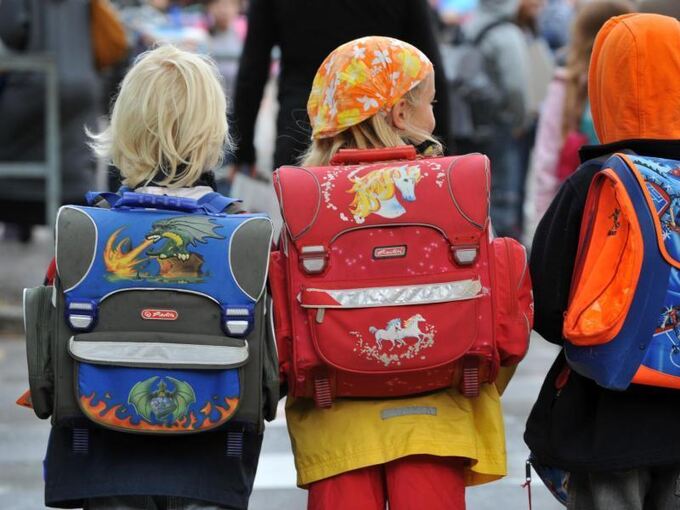 Drei Kinder laufen mit ihren Schulranzen zur Schule