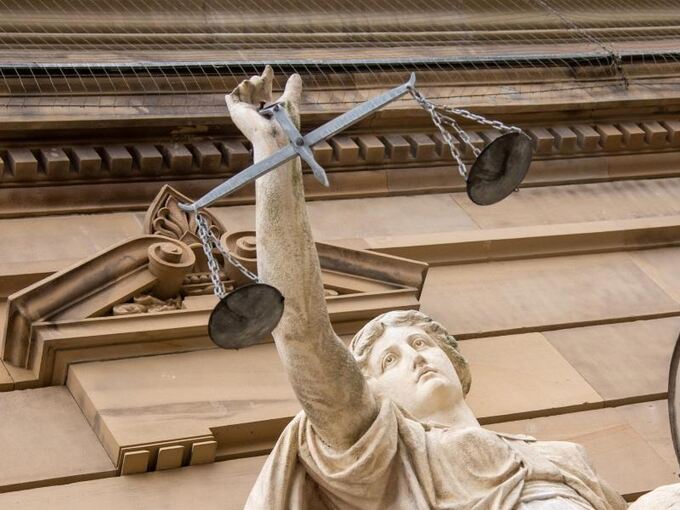 Vor einem Gericht hält eine Statue der Justitia eine Waagschale