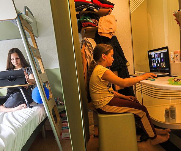 Die 13-jährige Maria verfolgt den Unterricht in der Heimat auf dem Hotelbett sitzend, ihre 9-jährige Cousine Vira sitzt neben der Dusche auf einem Hocker und nimmt ebenfalls am digitalen Unterricht ihrer Klasse teil. Trotz der ungünstigen Bedingungen