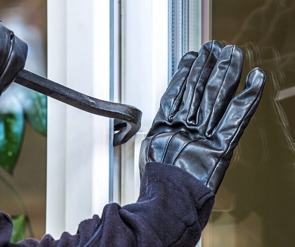 Ein Einbrecher hebelt ein Fenster auf. Symbolfoto: AdobeStock