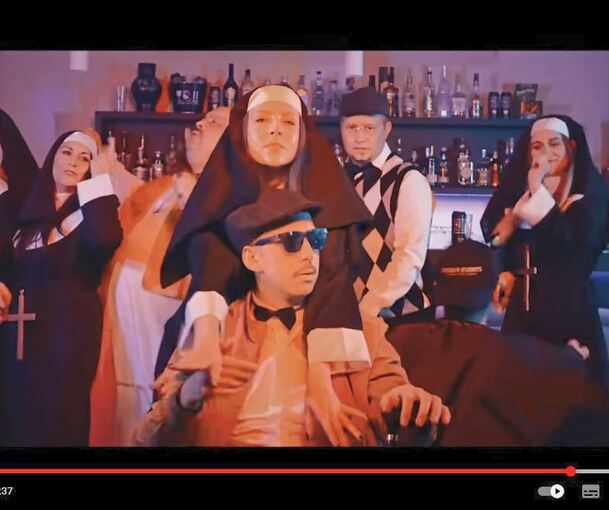 Videoszene mit DJ Robin (mit Brille), Schürze (karierter Pullunder) und „Nonnen“ in der entweihten Kirche bei Limburg. Screenshot/Video: Summerfield Records