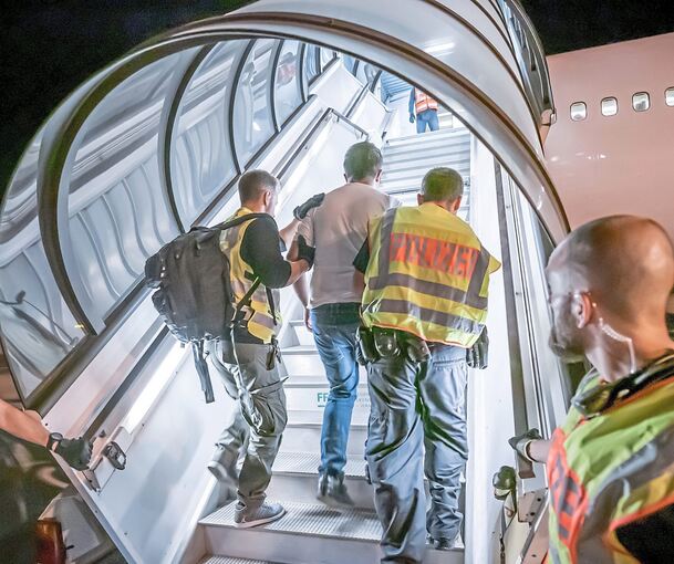 Polizisten begleiten einen Menschen, der abgeschoben werden soll in das Flugzeug (Symbolbild). Foto: dpa/Michael Kappeler (Archiv)