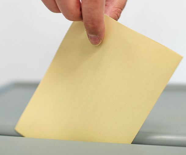 Ein Stimmzettel wird in eine Wahlurne geworfen. Symbol