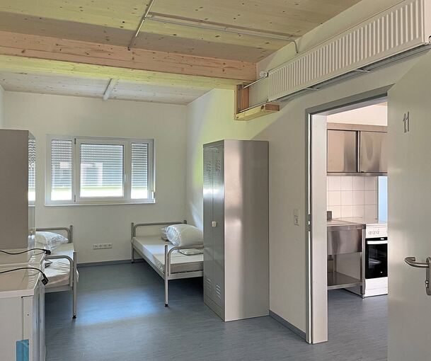 Blick in ein Vierer-Zimmer, dort hinein kommt man von einem Raum, der als Eingangsbereich und Küche dient, sowie als Zugang zu einem weiteren Viererzimmer und ins edelstahlverkleidete Bad.