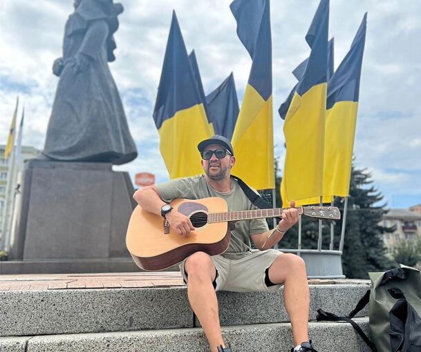 Das Foto, auf dem Jeff Mezak Jimenez Gitarre spielt, ist auf dem Unabhängigkeitsplatz in Riwnes Zentrum entstanden. Zu diesem Zeitpunkt hat eine Veranstaltung für die Gefallenen im Krieg stattgefunden.