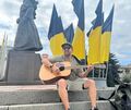 Das Foto, auf dem Jeff Mezak Jimenez Gitarre spielt, ist auf dem Unabhängigkeitsplatz in Riwnes Zentrum entstanden. Zu diesem Zeitpunkt hat eine Veranstaltung für die Gefallenen im Krieg stattgefunden.
