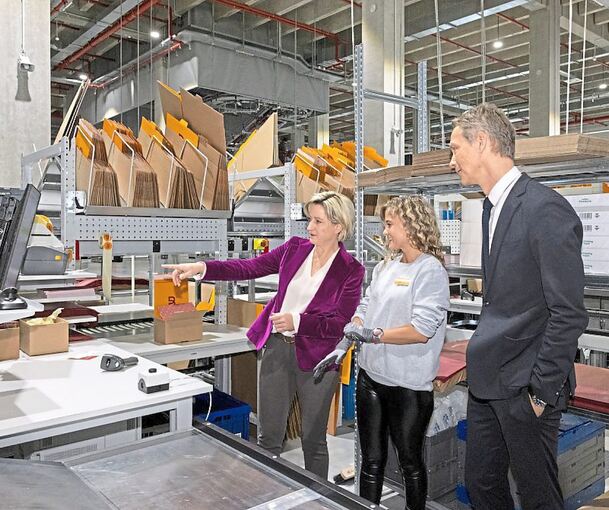 Wirtschaftsministerin Nicole Hoffmeister-Kraut (links) spricht beim Rundgang mit Breuninger-Chef Holger Blecker durch das erweiterte Warendienstleistungszentrum in Sachsenheim mit einer Mitarbeiterin in der Versandabteilung.