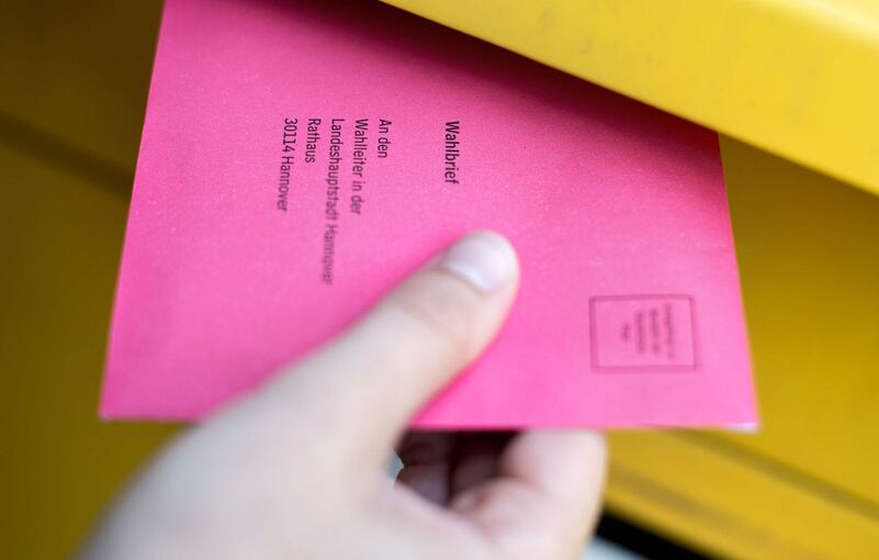 Frau steckt einen Wahlbrief in einen Postkasten Frau steckt einen Wahlbrief in einen Postkasten