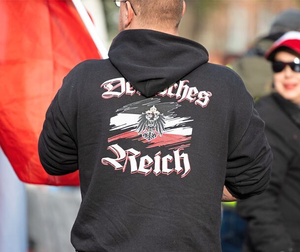 Ein Mann trägt einen Pullover mit dem Aufdruck „„Deutsches Reich“ bei einer Demonstration von Reichsbürgern.