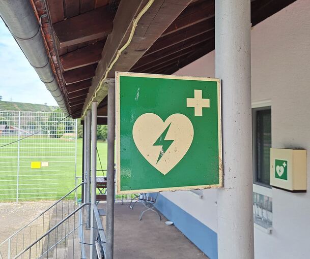 Ein Defibrillator kann Leben retten. Hier weist beim Sportplatz in Mühlhausen ein großes grünes Schild auf das Gerät an der Wand hin.