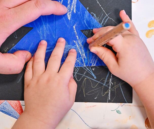 Eine Erzieherin unterstützt ein Kind beim Malen in einer Kita (Symboldbild). Damit es 2025/2026 genug Betreuungsplätze in Freudental gibt, muss die Gemeinde einiges unternehmen.