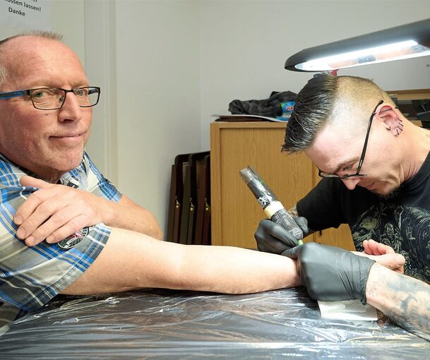 Manfred Eberlein lässt sich von Markus Melon das Schaf aufs Handgelenk stechen.