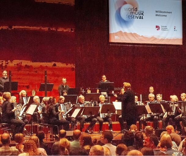 Ein Banner des World Music Festival Innsbruck ist in der ecke oben rechts, zu sehen ist außerdem das Orchester mit Leitung von D