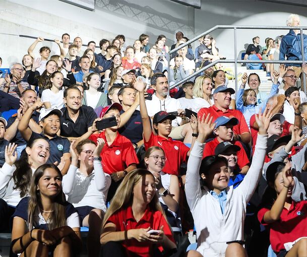 Viele Kinder und Jugendlichen sitzen in einem Bild. Manche heben die Hände und klatschen.