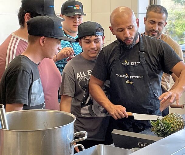 Geduldig erklären Craig Taylor und Schulbauernhof-Koch Eddy, wie man die einzelnen Gerichte zubereitet, hier, wie man eine Ananas für den Cocktail schneidet.