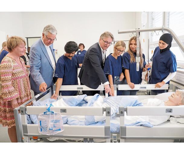 Minister Manfred Lucha (Mitte) im „Skills Lab“ an einem Pflegebett. Hier üben die Auszubildenden den Umgang mit Patienten.
