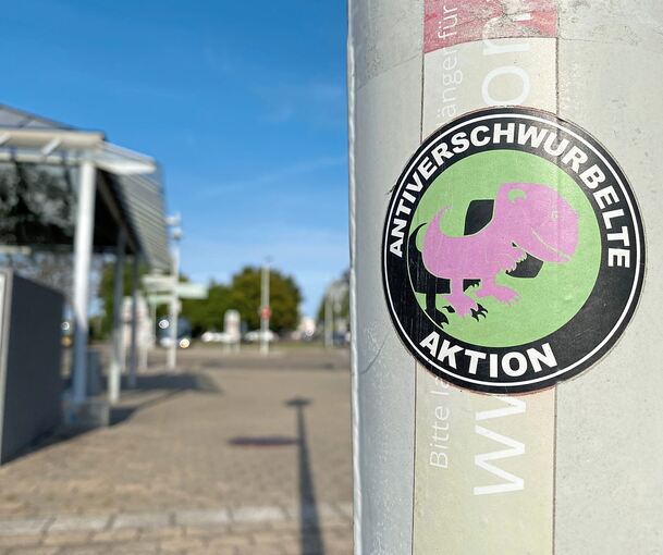 Ein überklebter Sticker von Corona-Leugnern erinnert an die enorme Belastung zu Pandemiezeiten und den Widerstand einiger Gruppen gegen die Gesundheitspolitik.
