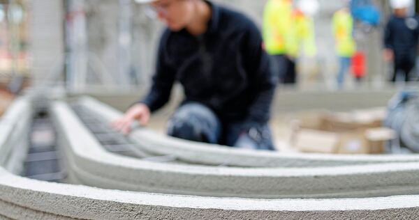 Eine Mitarbeiterin betrachtet übereinandergeschichtete Betonstreifen, die von einem seriellen 3D-Gebäudedrucker gesetzt wurden.  Eine Mitarbeiterin betrachtet übereinandergeschichtete Betonstreifen, die von einem seriellen 3D-Gebäudedrucker gesetzt wurden.