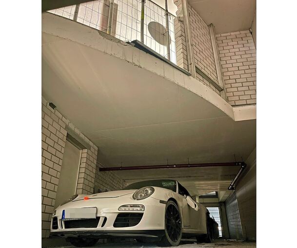 Die Feuerwehr hat den Porsche mit Hebekran abgeseilt und auf die Räder gestellt. Darüber ist die Absturzstelle zu sehen. Das Loch in der Ziegelwand ist mit Gitter, Streben und Sichtschutz gesichert.