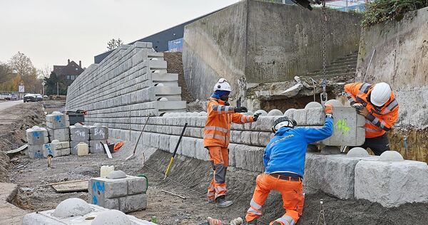 Bauarbeiter setzen die Betonteile der neuen Valeo-Stützmauer zusammen, dabei helfen ihnen aufgesprühte Nummern.