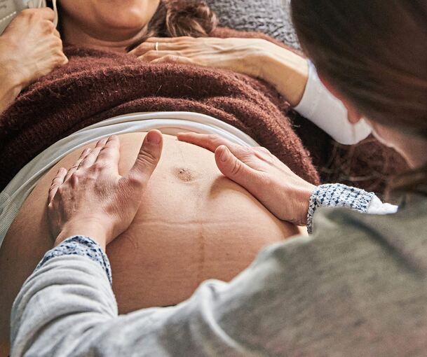 Eine Hebamme tastet den Bauch einer schwangeren Frau ab.