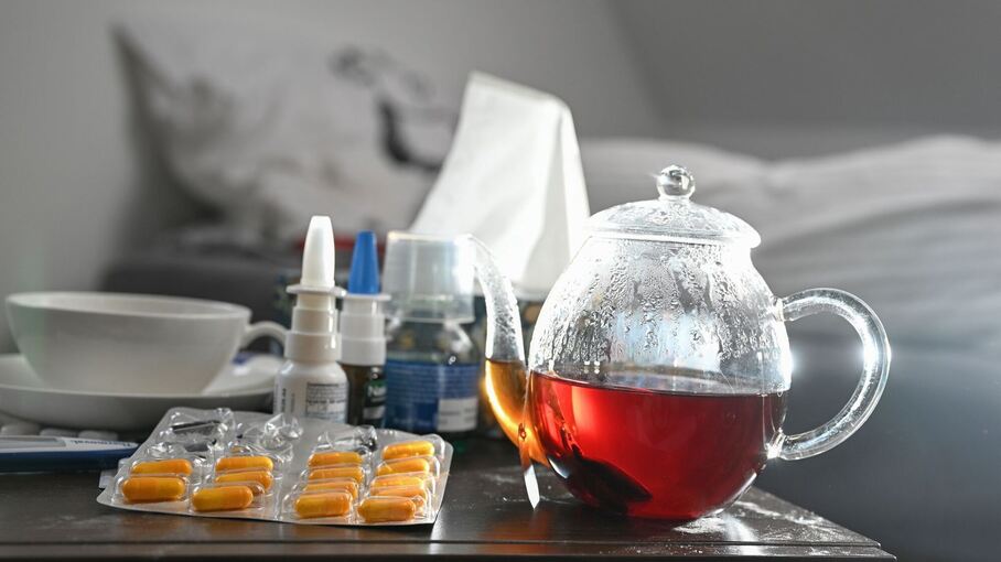 Medikamente und eine Kanne Tee auf einem Nachttisch
