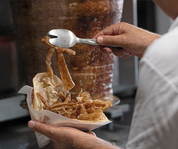 Ein Mann füllt ein Fladenbrot mit Fleisch von einem Dönerspieß. Der Spieß wurde von der Firma Birtat produziert.