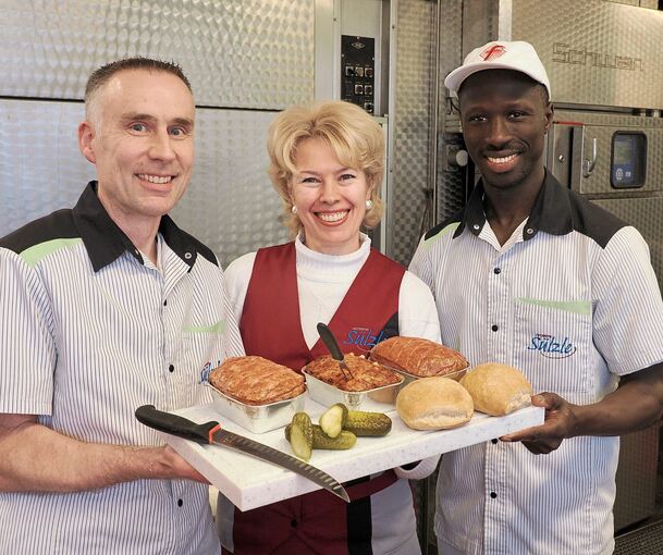 Stefan und Ludmila Sülzle präsentieren gemeinsam mit Lamin Manneh den fertigen Fleischkäse.
