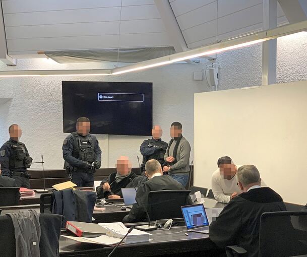 Die beiden Angeklagten G. und I. betreten in Begleitung von Justizbeamten den Gerichtssaal, K. (rechts) kommt als freier Mann durch den Eingang.