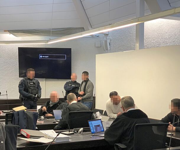 Die beiden Angeklagten G. und I. betreten in Begleitung von Justizbeamten den Gerichtssaal, K. (rechts) kommt als freier Mann durch den Eingang.